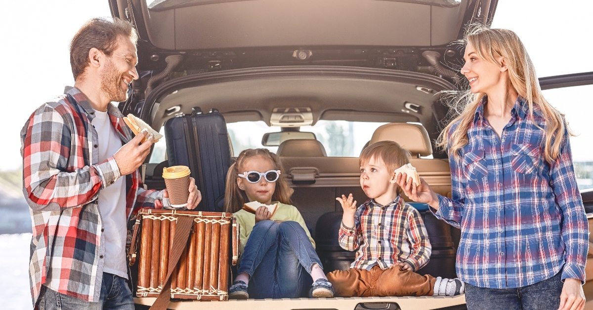 family stands near the car having a lunch