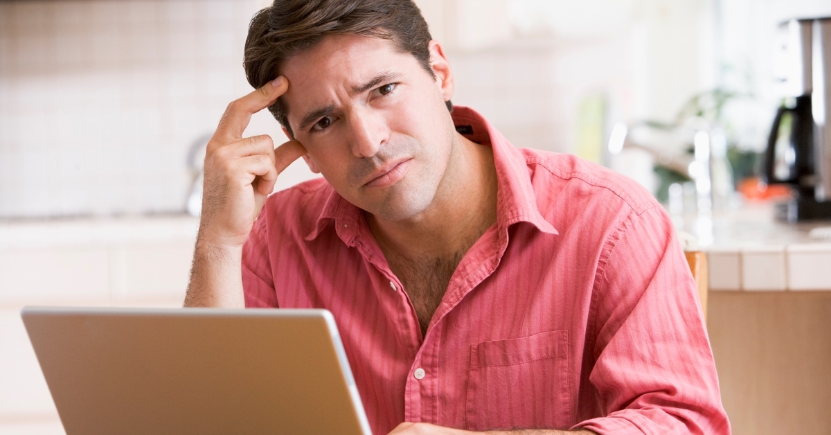 man in kitchen using laptop frowning
