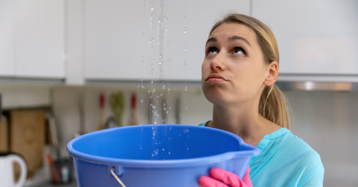 woman collecting water in bucket leaking from roof