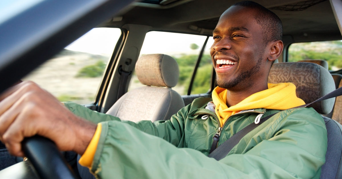 smiling african american man driving car while wearing seatbelt during day time