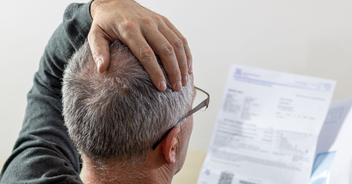 senior man drops his hand to his head in shock seeing his bills