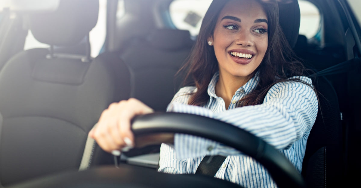 happy young woman sitting in driver seat with hands on steering wheel