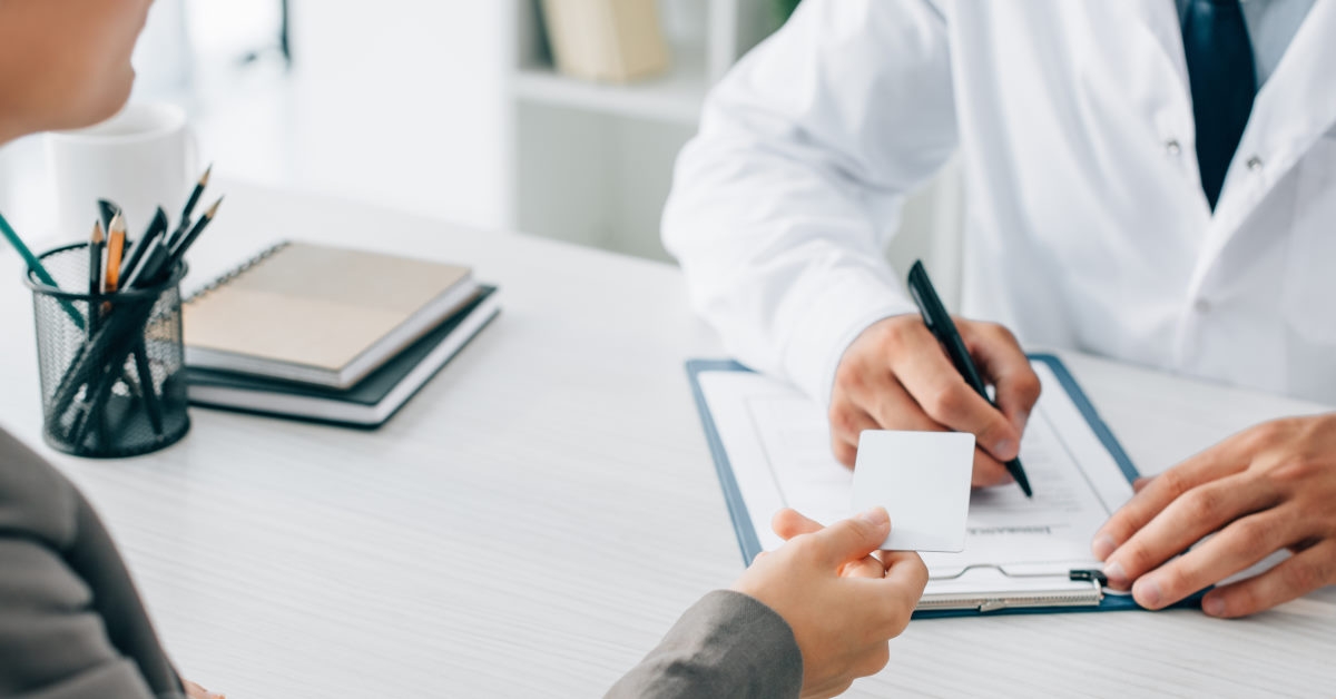 patient giving card to doctor who is writing on notepad