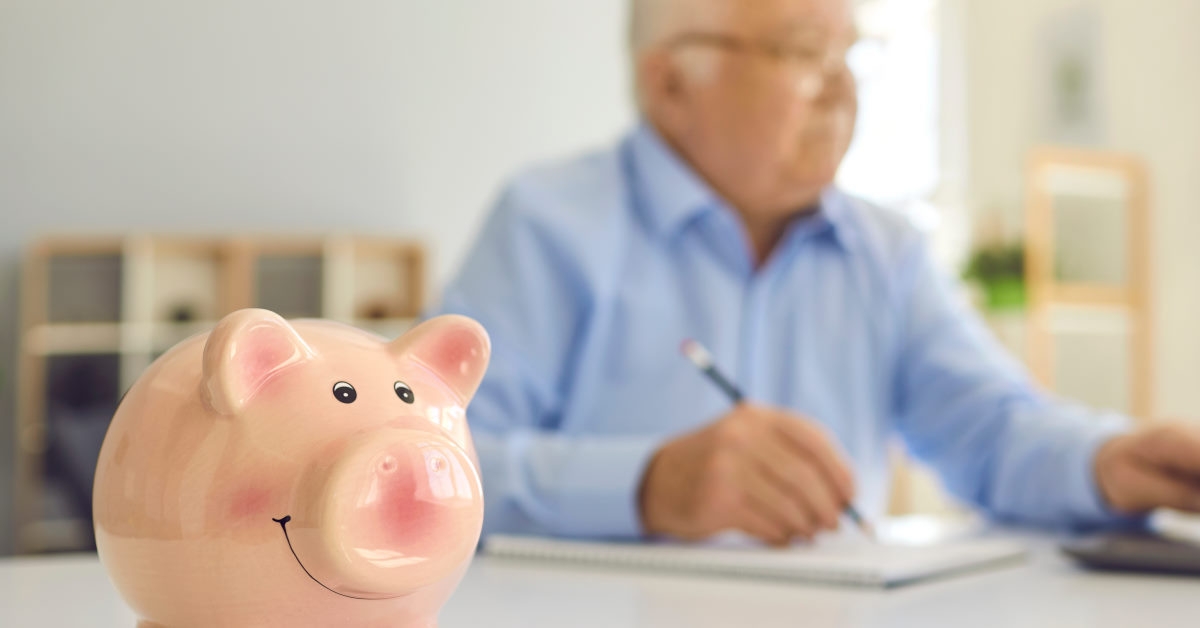 senior man working at office in background with piggy bank and pennies on table