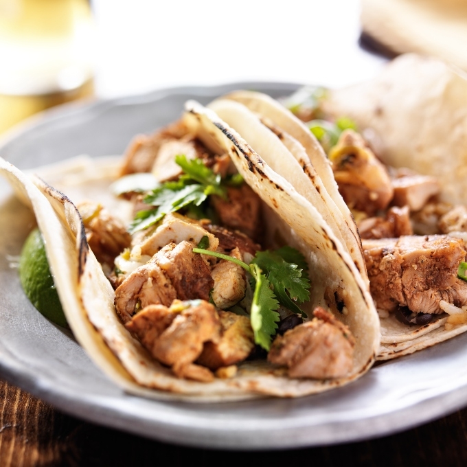 Two chicken tacos with soft tortillas and cilantro on a plate