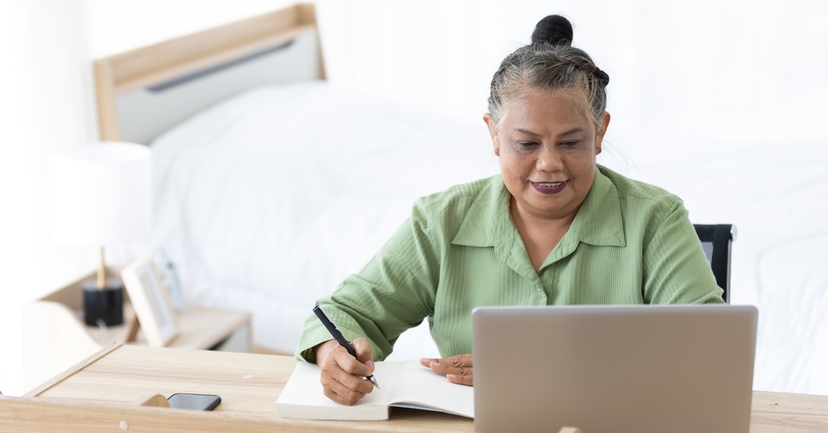 senior woman writing in notebook and using laptop