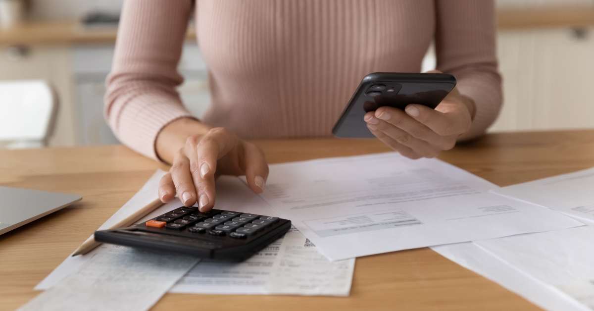 woman uses phone and calculator to manage financial documents