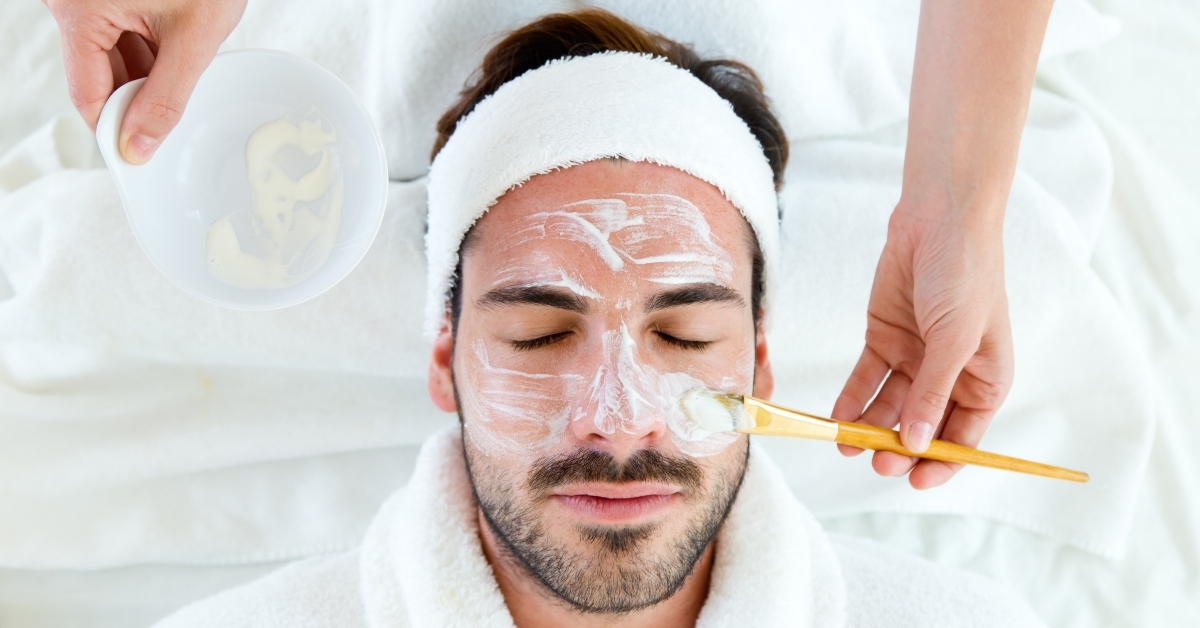 man with clay facial mask in beauty spa