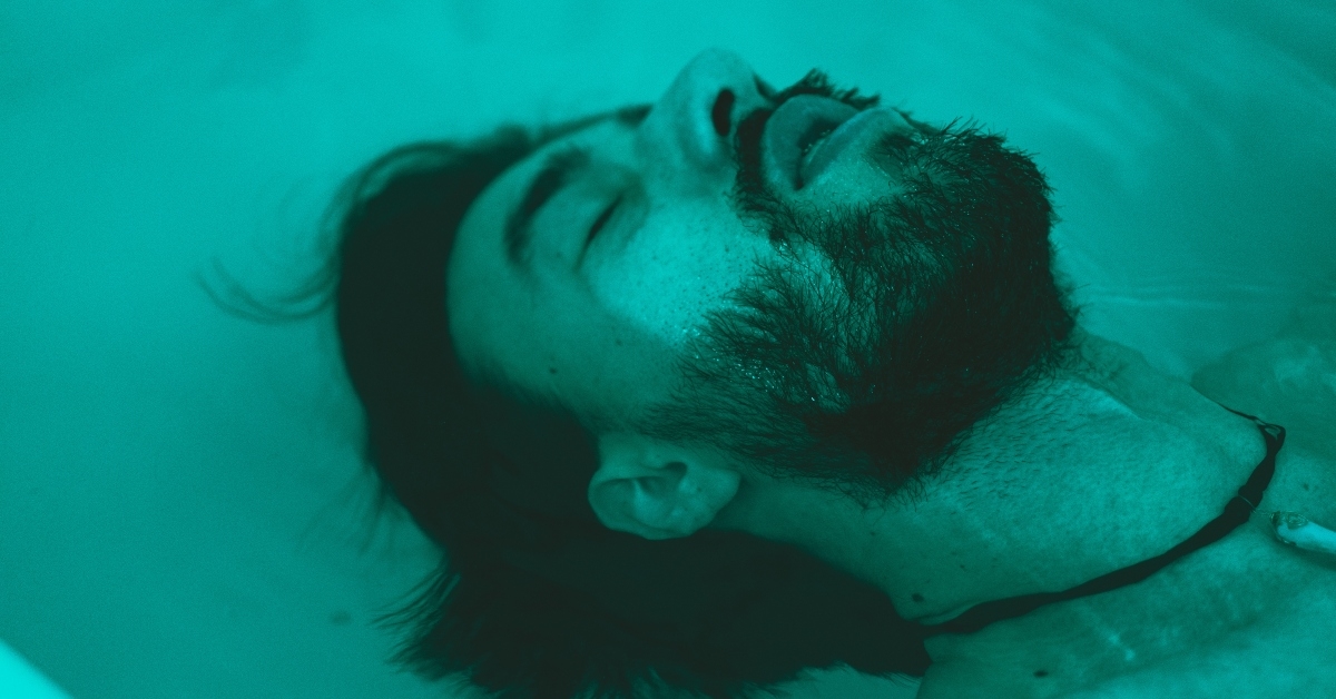 close up bearded men with eyes closed floating in flotation therapy cocoon 