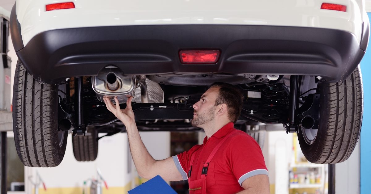 man checking car from underneath while holding paperboard