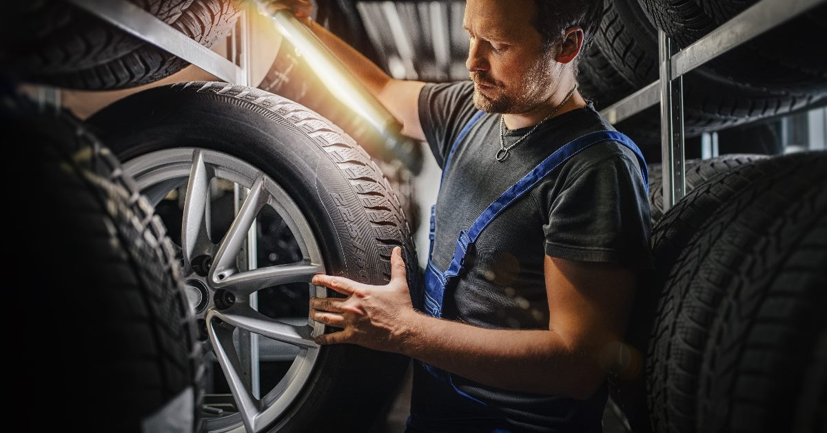mechanic using light to inspect car wheels at warehouse