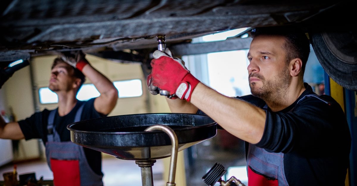 mechanics at workshop changing oil in car