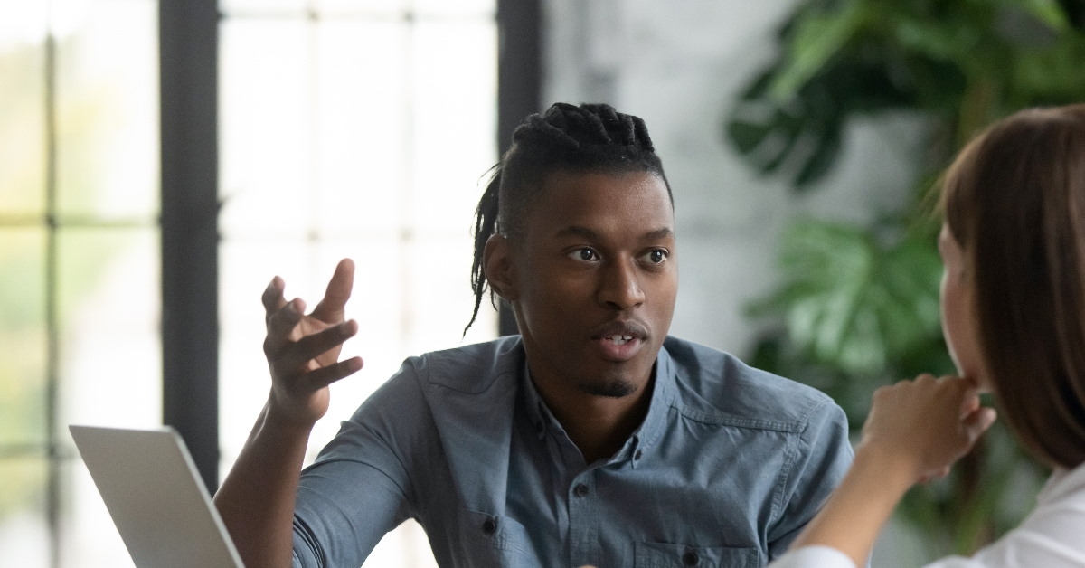 african american man talking to young female colleague sitting in front of laptop
