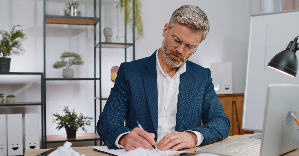 senior employee writing on notepad in front of laptop