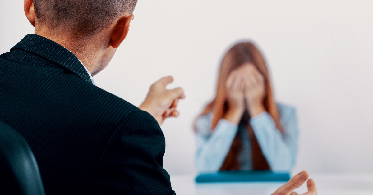 young female colleague covering her face as the boss scolds her across the table