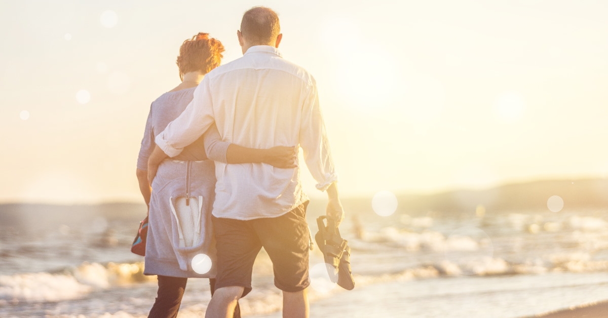 senior couple holding each others back walking down the sea coast 