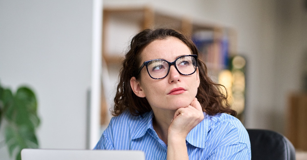 young woman sitting in office thinking in front of laptop on table