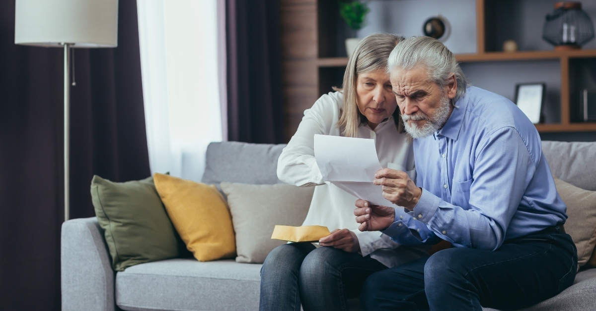 senior husband showing banking paper to confused elderly wife