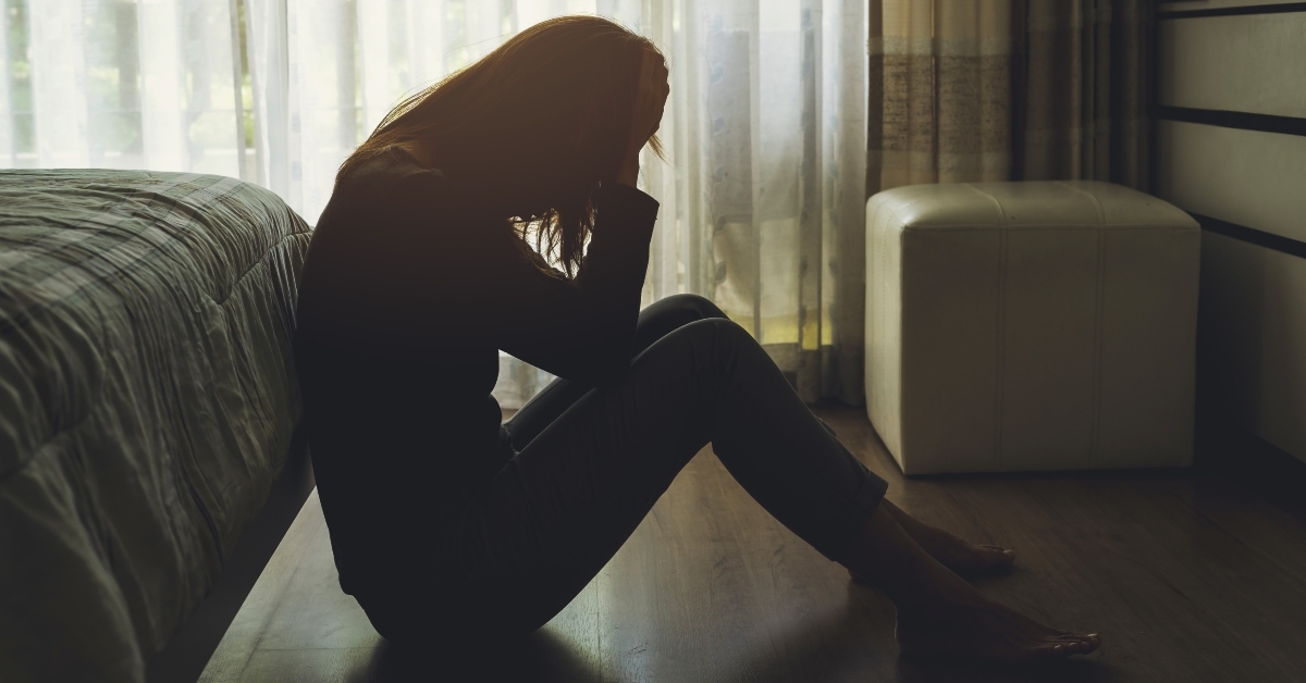 depressed woman sitting with head in hands in the dark bedroom