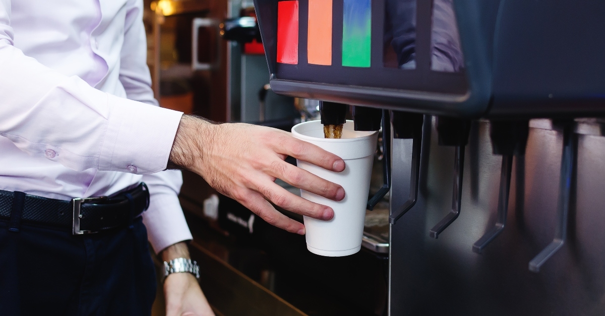 man pours a fizzy drink into a paper cup from a cola machine