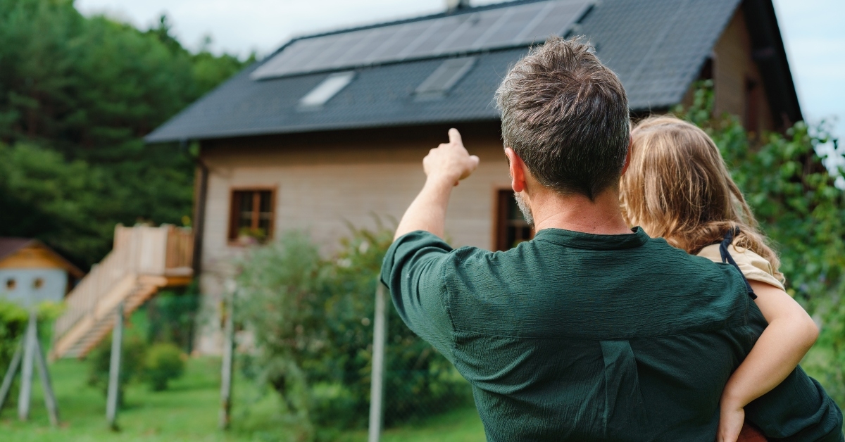 dad holding her little girl in arms and showing their house