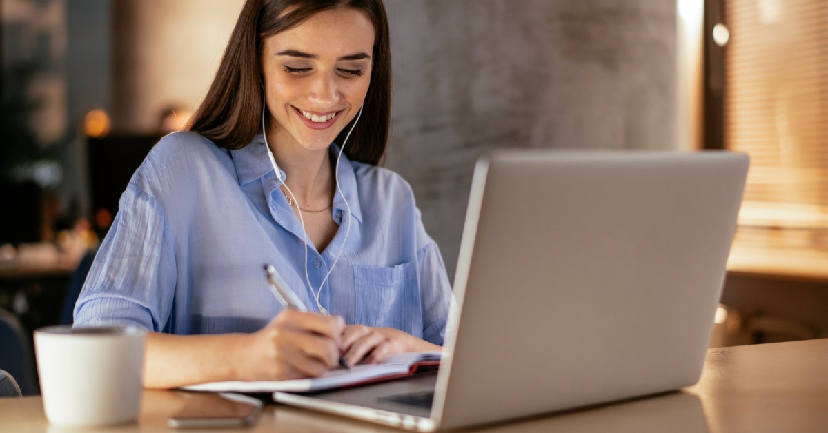 happy woman sitting in front of laptop writing on notebook