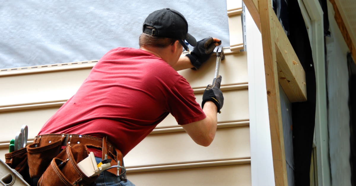 male worker standing on ladder to forge nails using hammer