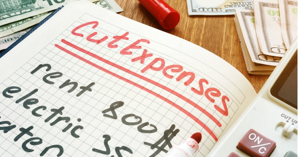 calculator and notepad with cut expenses written with red marker 