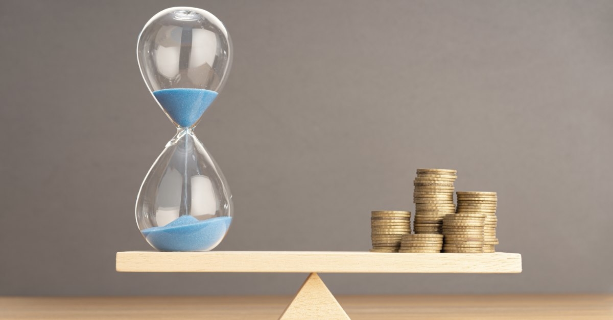 sand clock and stack of pennies balancing on seesaw in front of grey background