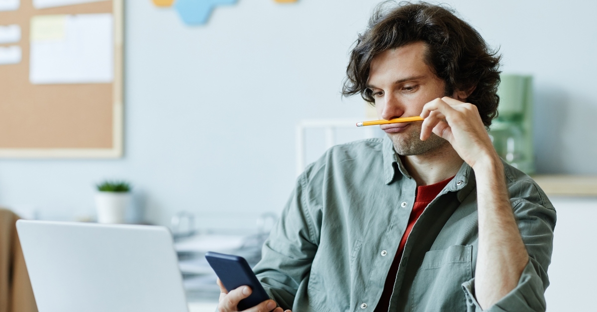 bored man playing with pencil and using phone at workplace