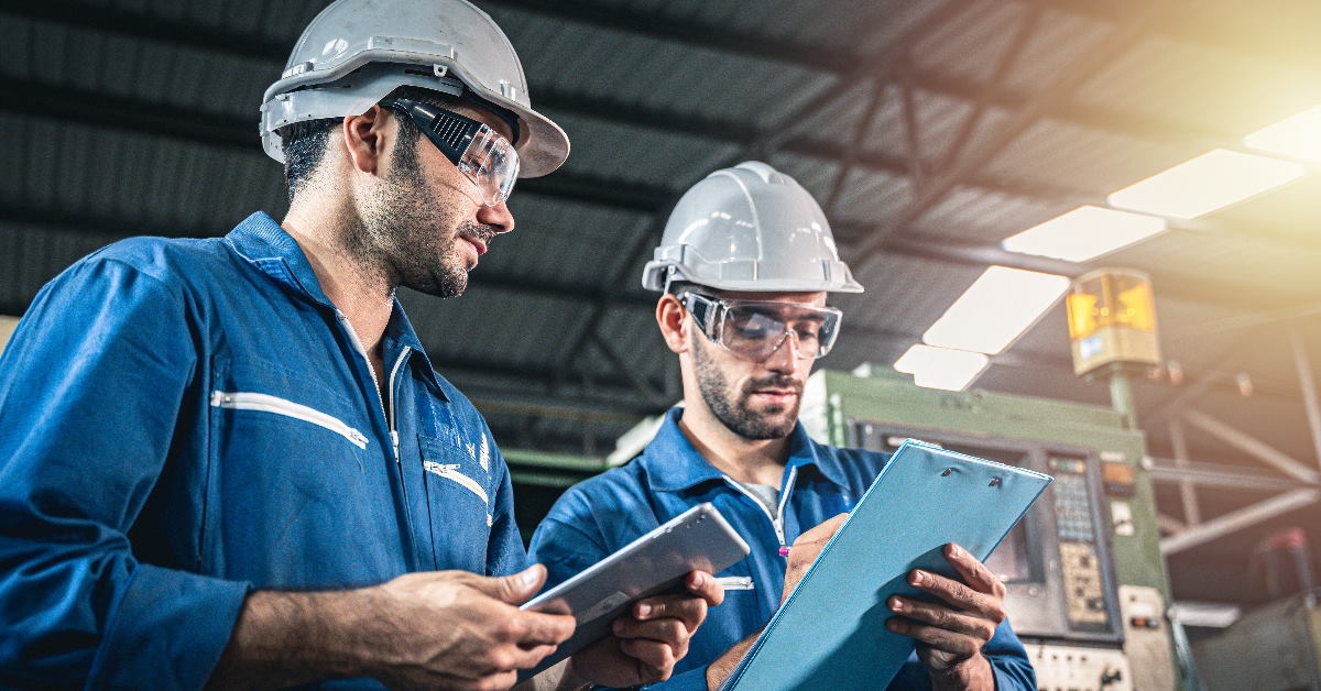 engineers at work site wearing safety gear checking out maintenance documents on clipboard in hands
