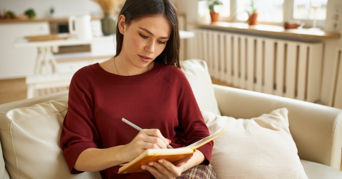 female with dark haired sitting on comfortable couch holding pen