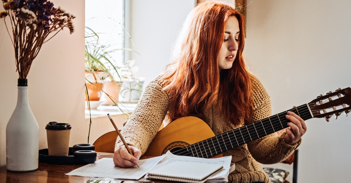 red-haired woman in sweater playing acoustic guitar