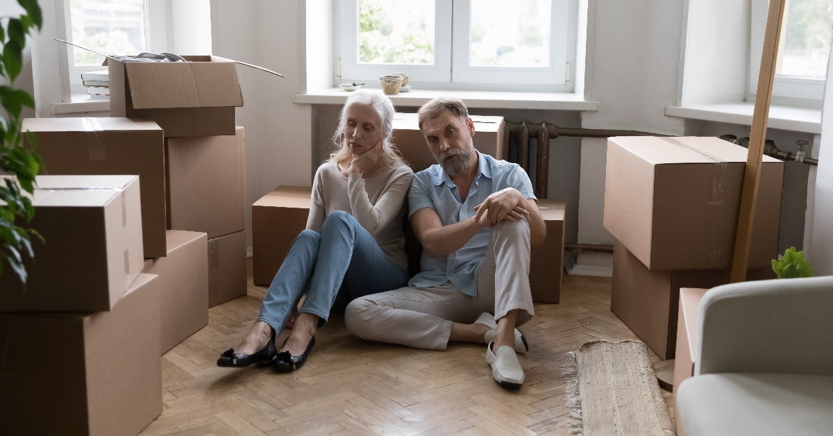 senior couple tired after relocation sitting on floor with lots of moving boxes