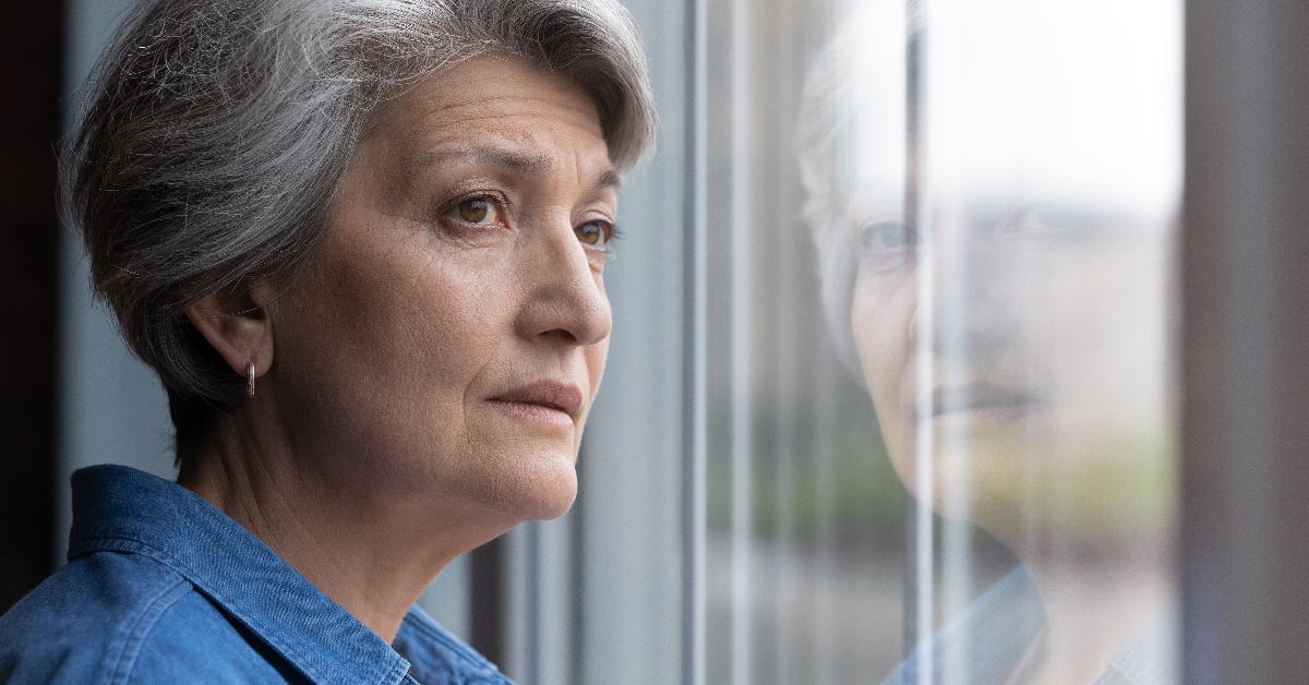 senior lady with short hair standing at home looking outside window