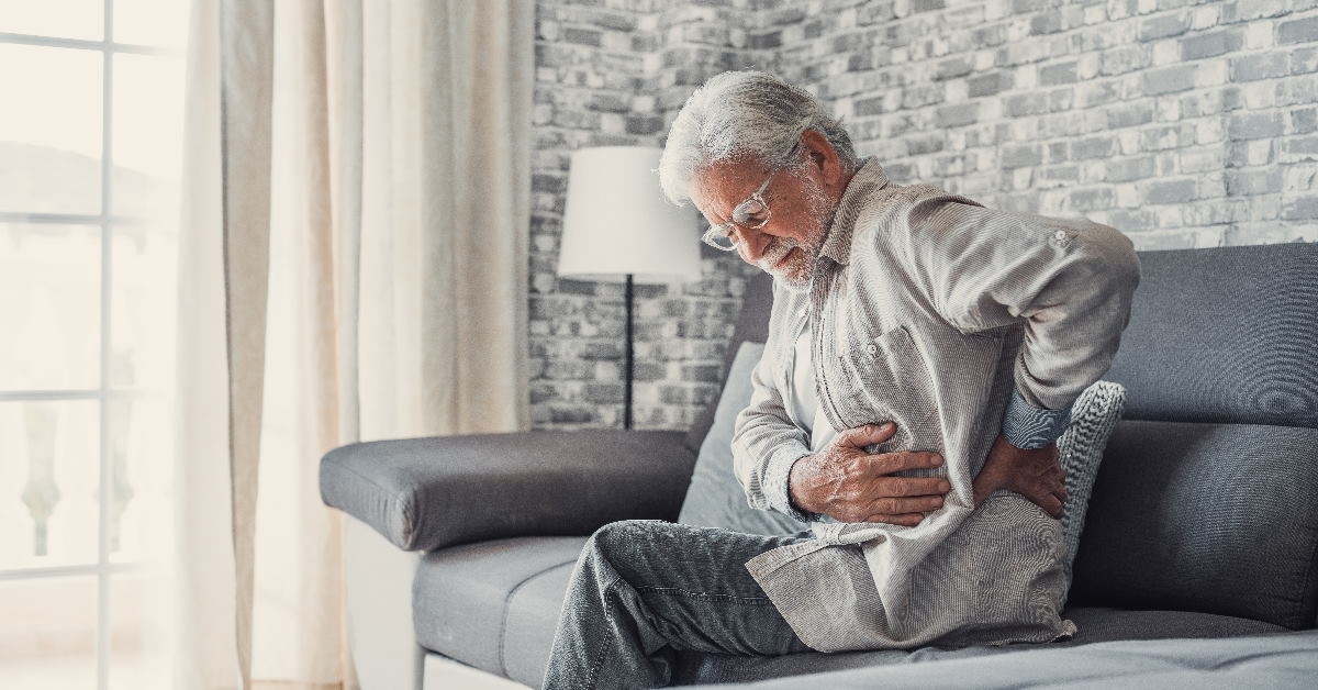 senior man holding his back due to back ache sitting on couch at home