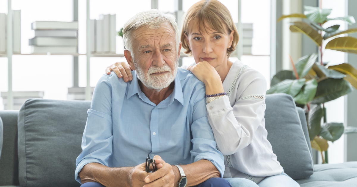 senior couple sitting together on couch at home lost in deep thoughts