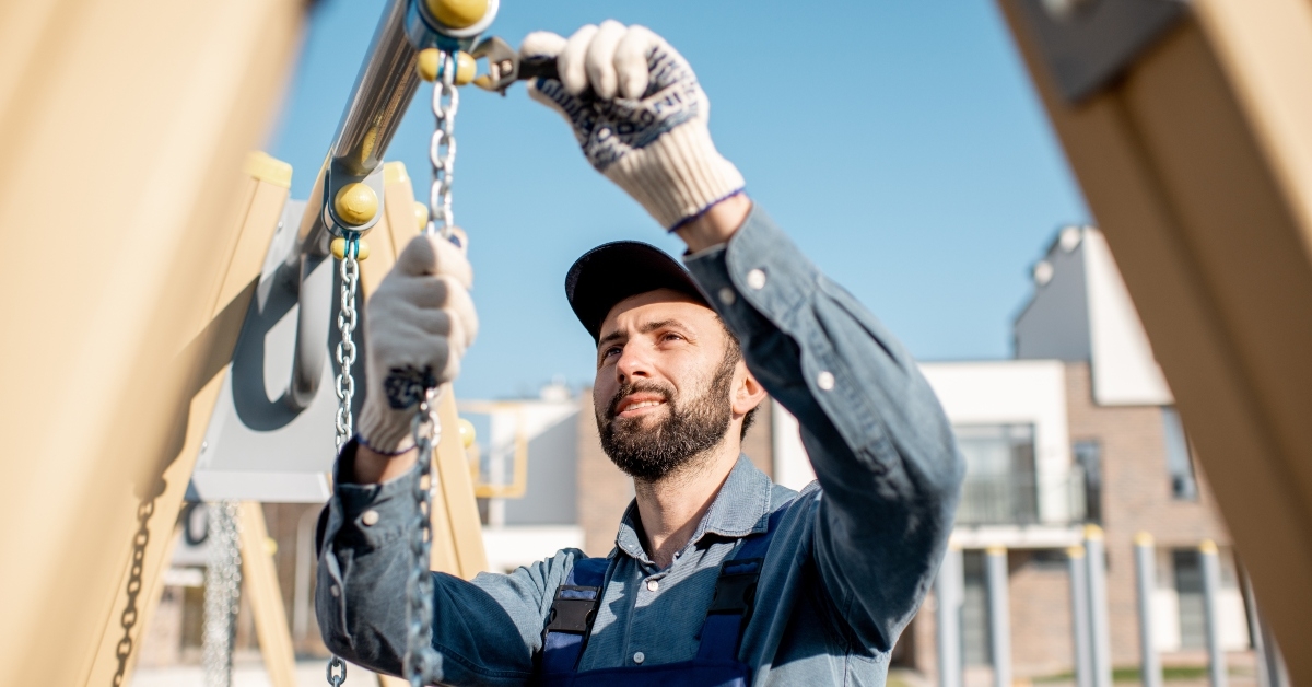 workman in uniform mounting swing on the playground