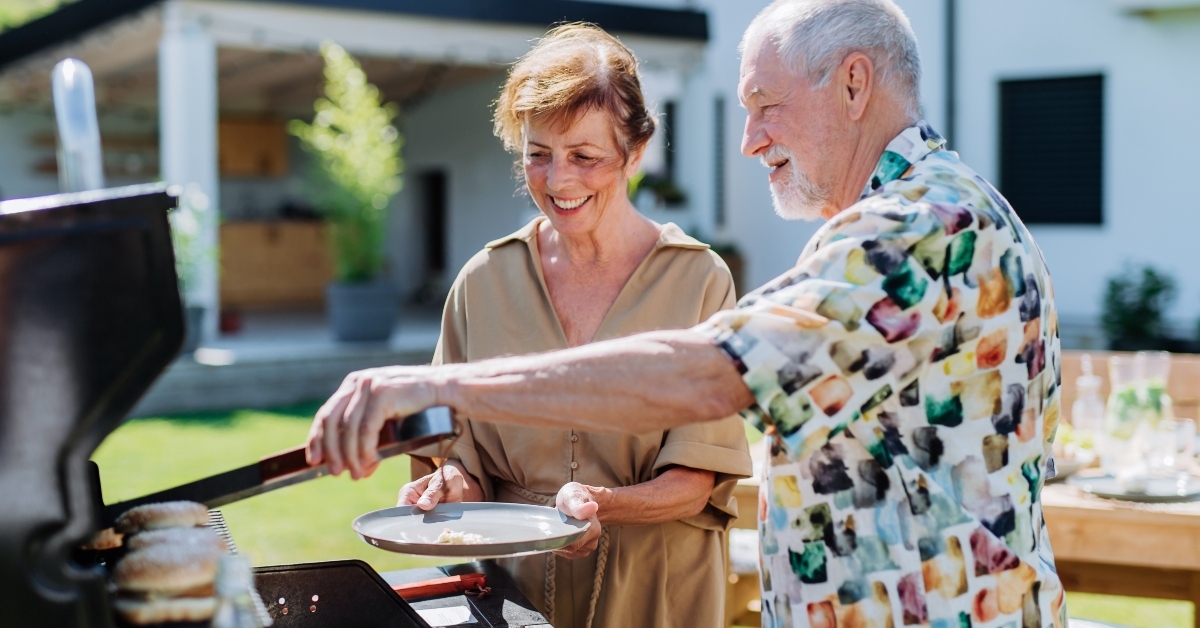 senior man grilling outdoor giving his wife hamburger