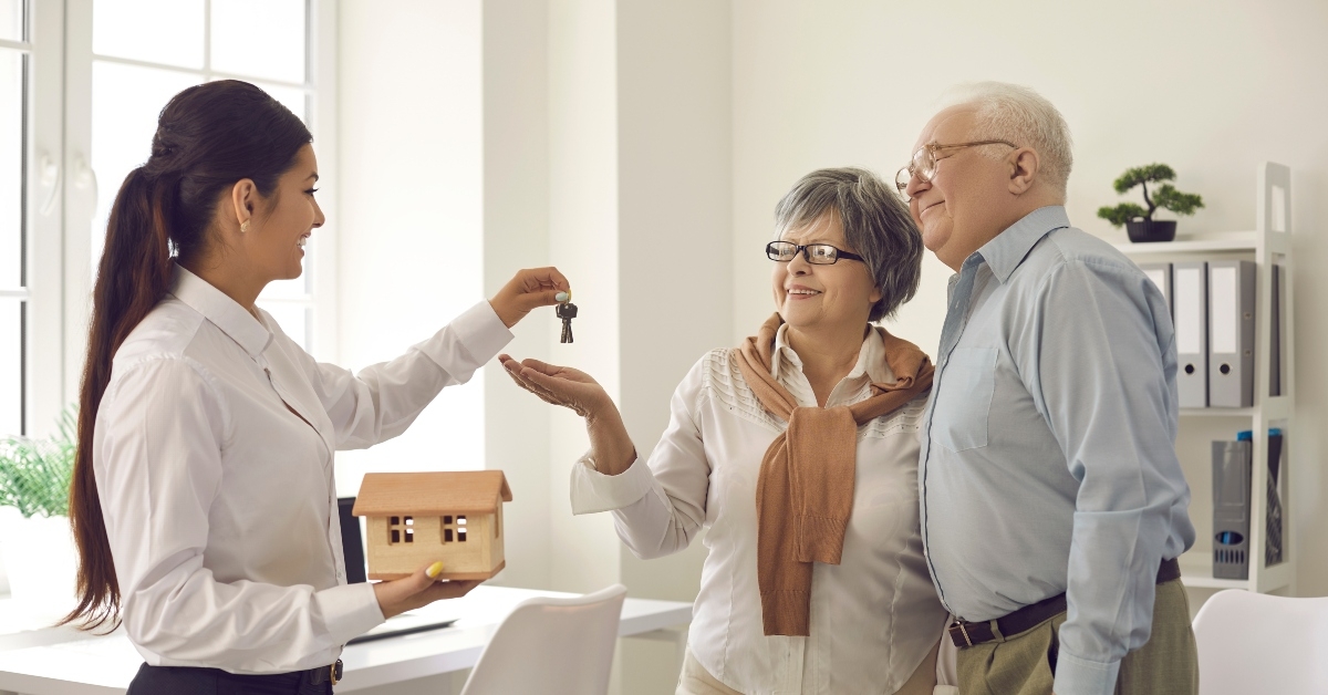 female real estate agent give keys to elderly couple