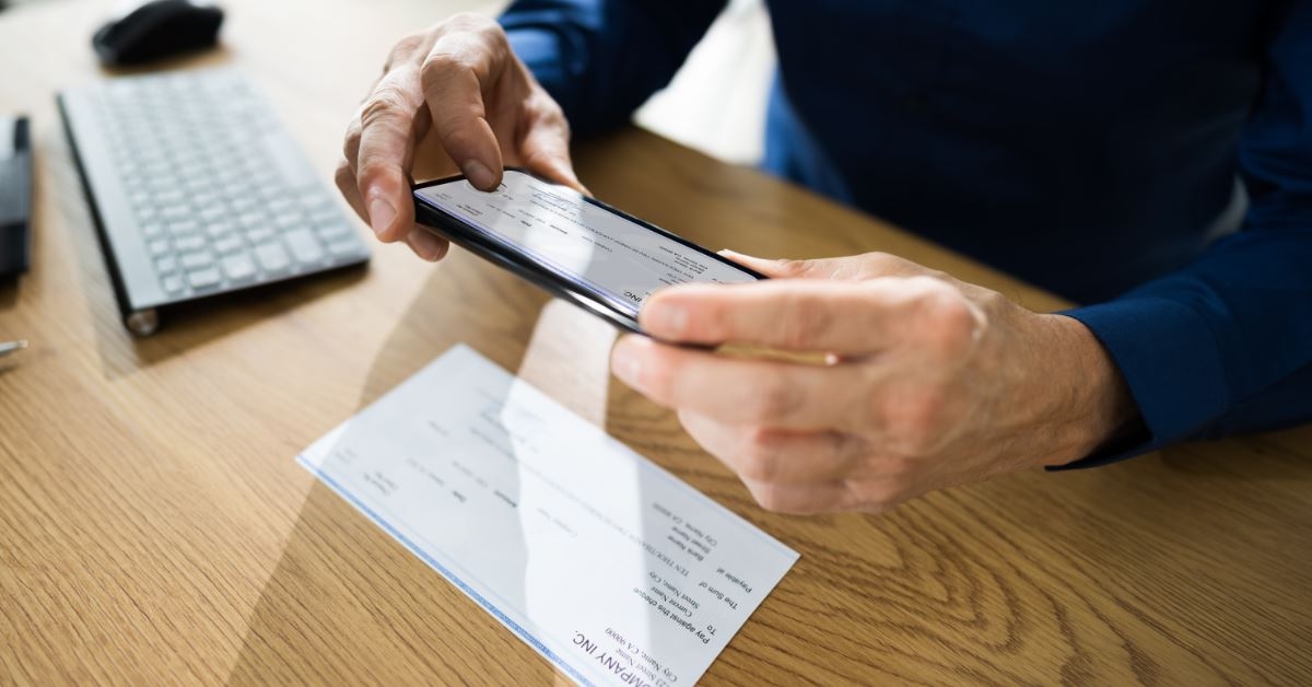man using smartphone to click picture of check deposit at wooden table