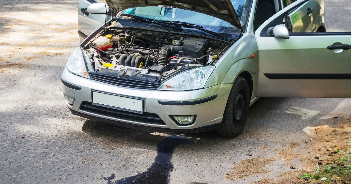 car stranded in the middle of road with doors open as oil is leaking out of it