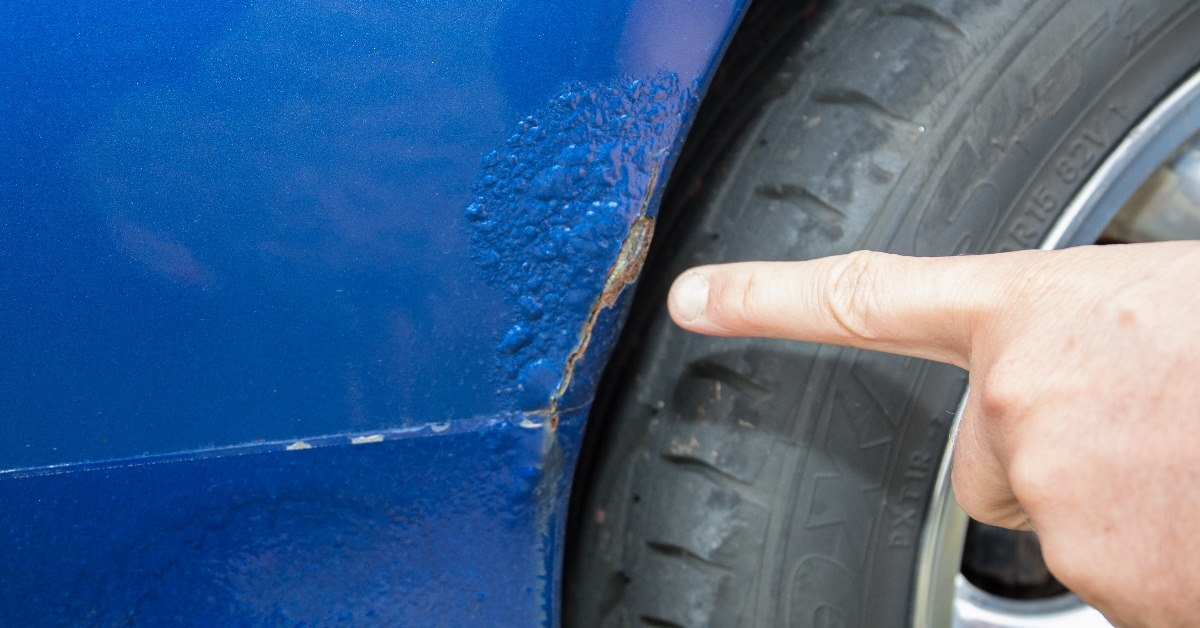 finger pointing rust damaged part of car near the wheels
