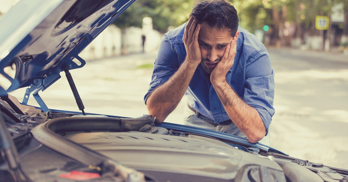 man in formal dressing looking at broken car engine in stress on road