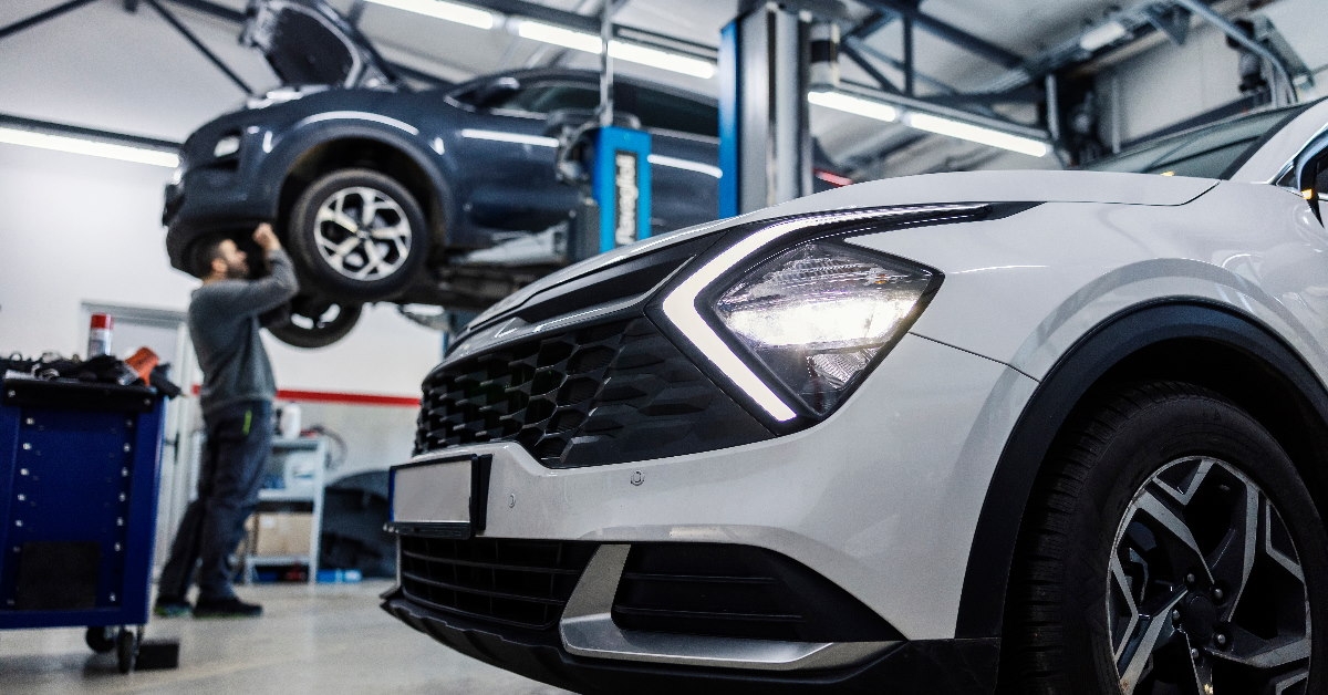 mechanic repairing car in automobile workshop from beneath with another white car at front
