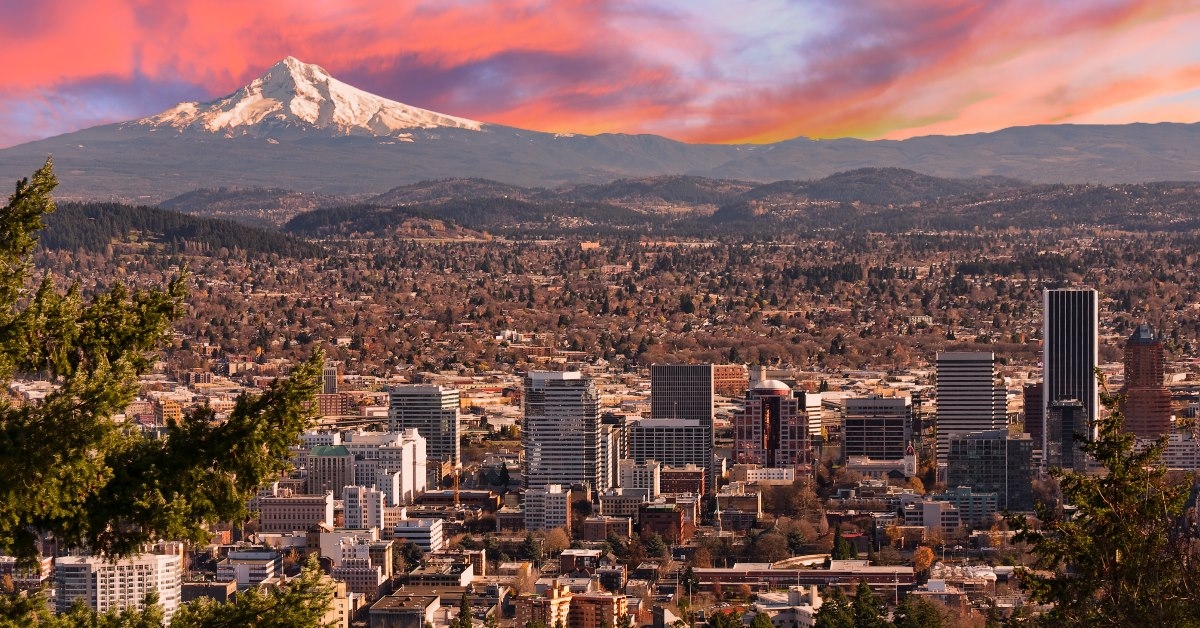 beautiful vista of portland with bunch of buildings and snowy mountain in the background under violet sky