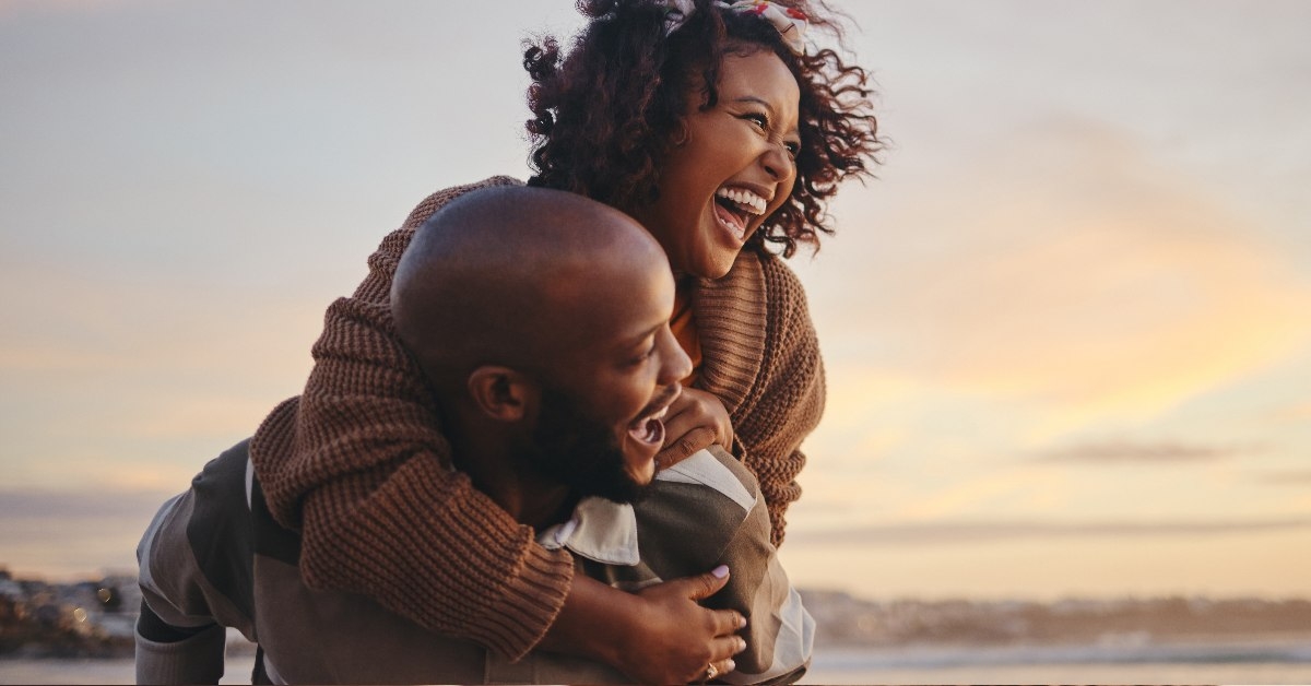 african american couple enjoying piggy ride while walking on beach