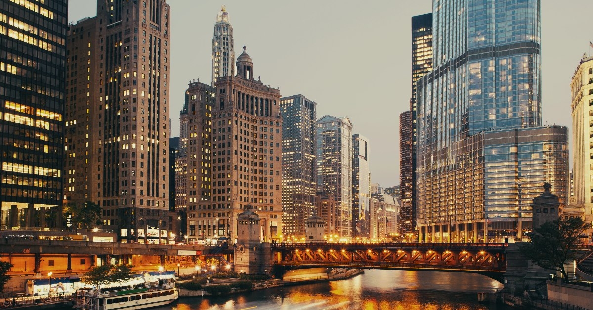 dusable bridge on water with boats in the middle of skyscrapers with golden lights in chicago