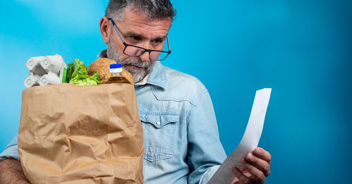 man looking at receipt in hand while holding brown grocery bag