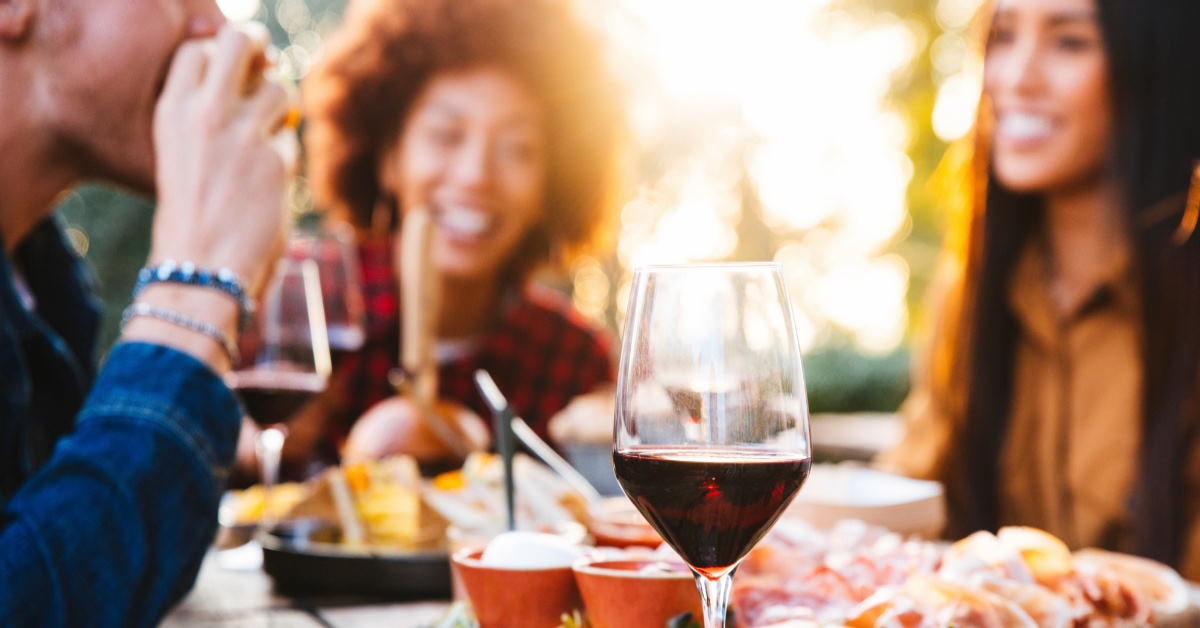 friends sitting at table in restaurant with food and red wine glass